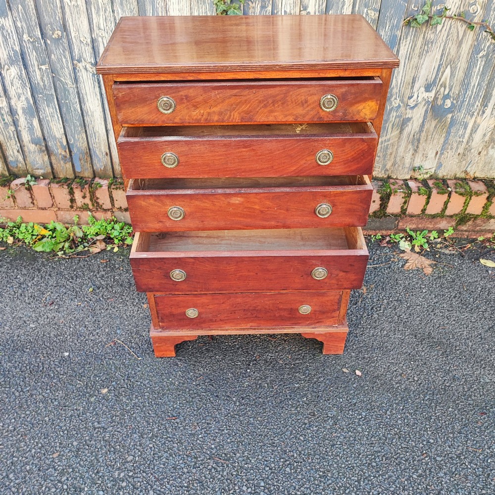 A tall, narrow mahogany chest of six drawers with circular brass ring pulls, flame veneer drawer fronts, and bracket feet. View II