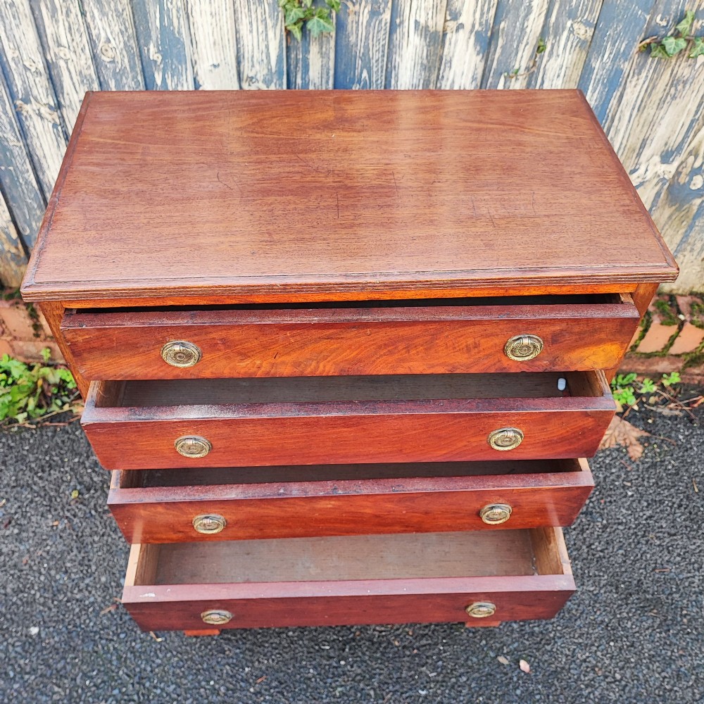 A tall, narrow mahogany chest of six drawers with circular brass ring pulls, flame veneer drawer fronts, and bracket feet. View VI