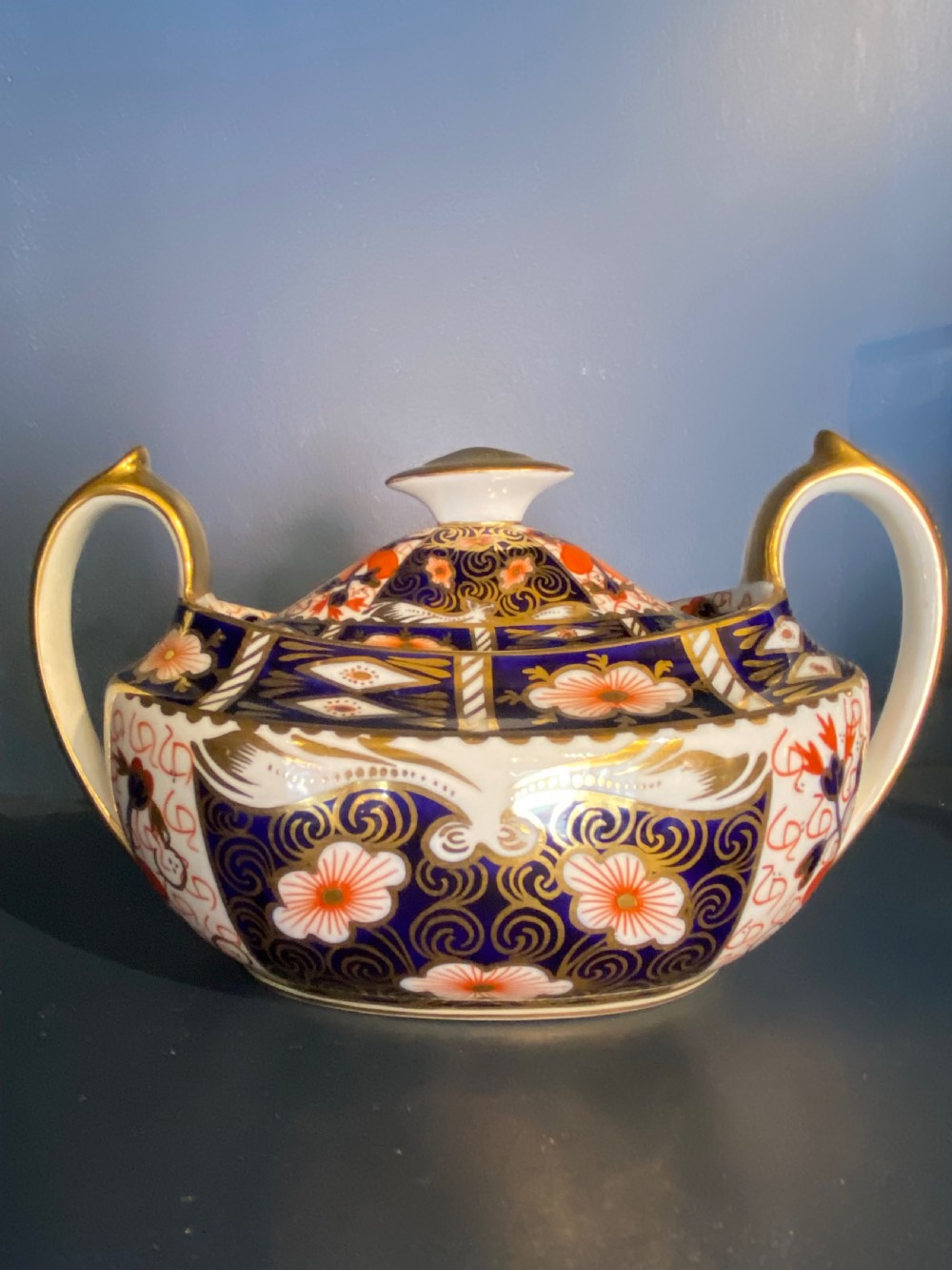An antique Royal Crown Derby porcelain covered sugar bowl with twin handles, decorated in cobalt blue, iron red, and gilt Imari patterns.