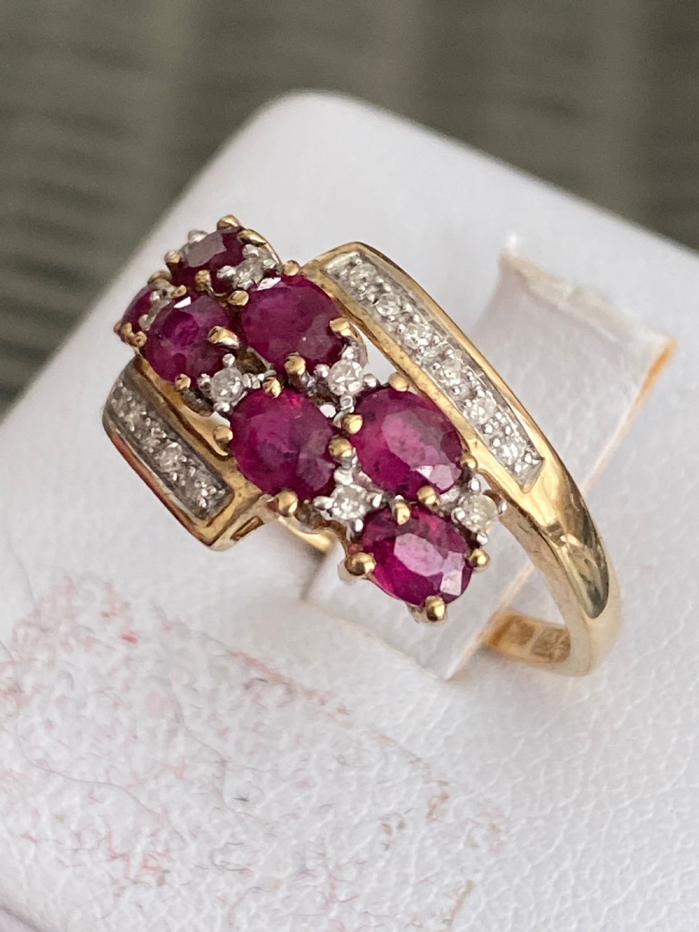 A vintage yellow gold dress ring featuring multiple oval cut rubies alongside small diamond accents set within curved gold rails. View III