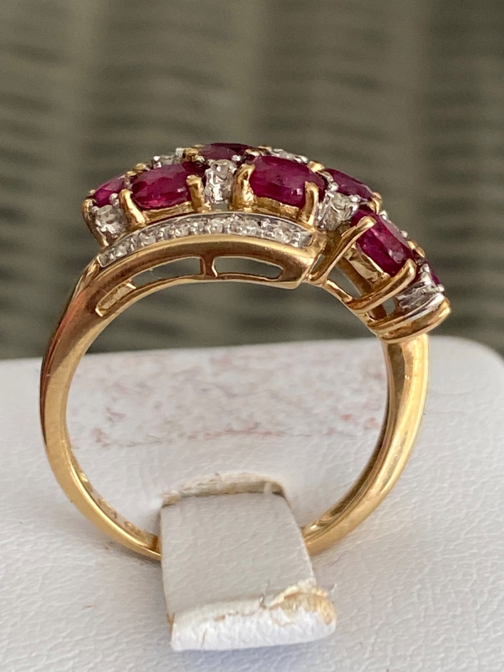 A vintage yellow gold dress ring featuring multiple oval cut rubies alongside small diamond accents set within curved gold rails. View IV