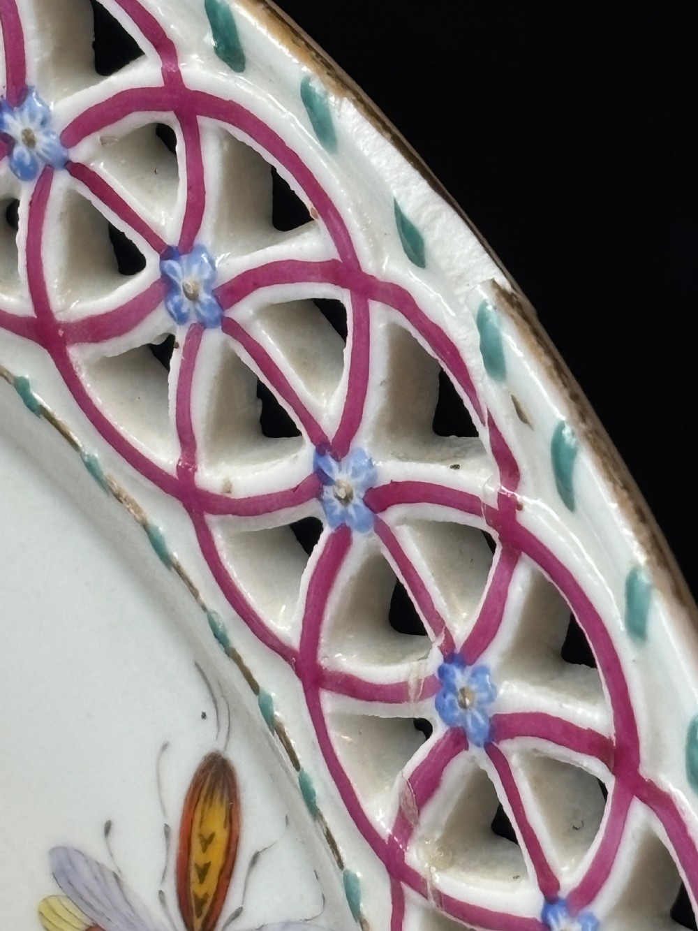 A circular porcelain plate featuring a pink reticulated lattice rim and a hand-painted central botanical scene with flowers and insects. View II