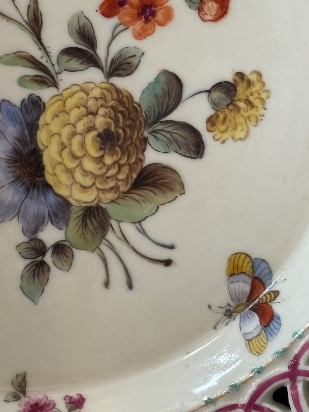 A circular porcelain plate featuring a pink reticulated lattice rim and a hand-painted central botanical scene with flowers and insects. View IX