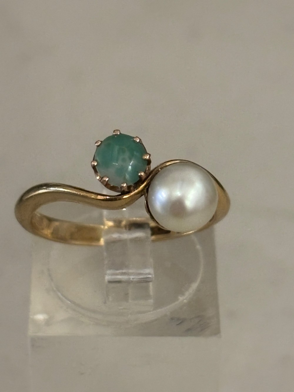 A yellow gold bypass ring featuring a round white cultured pearl alongside a claw-set green jade cabochon.