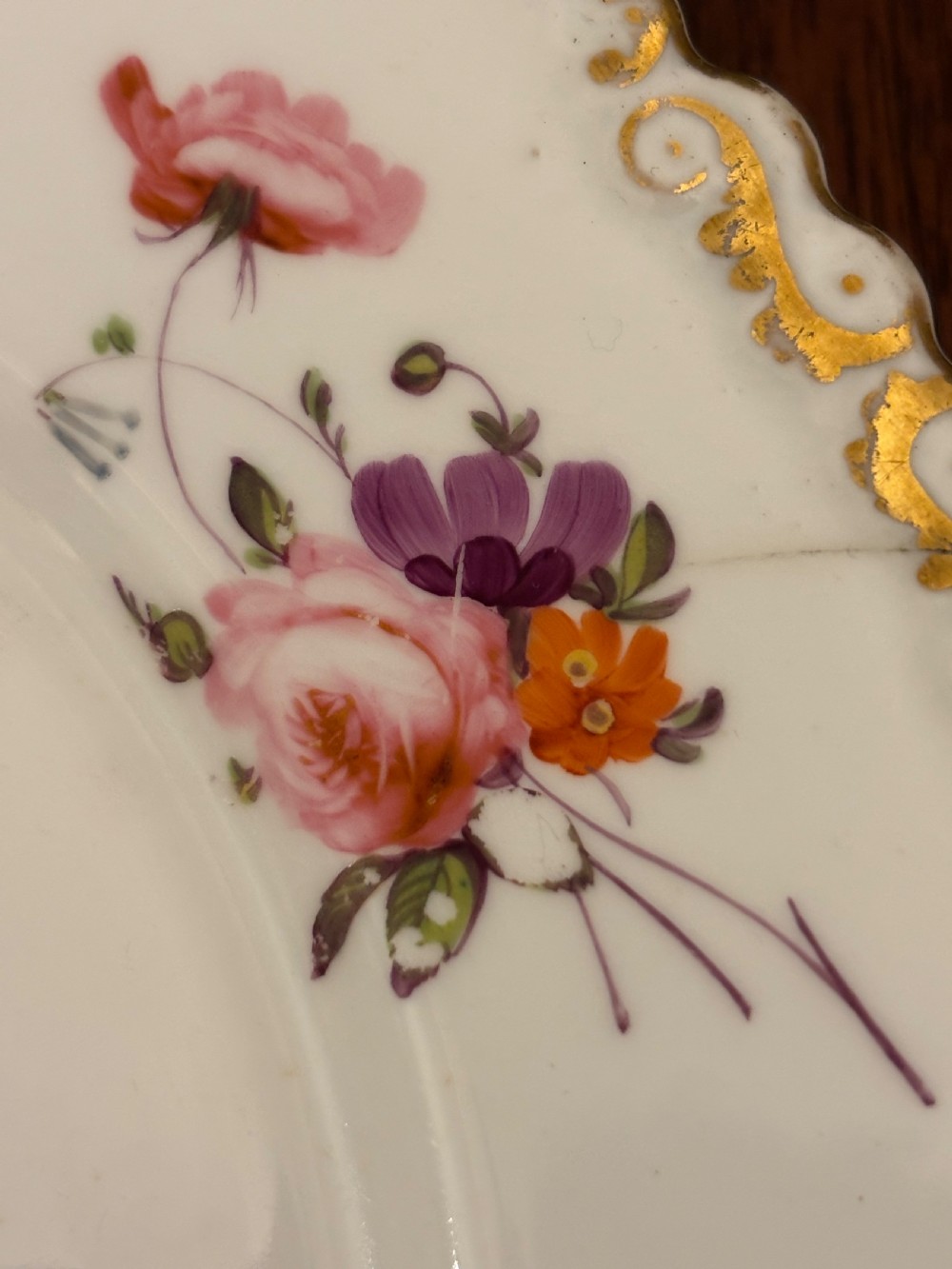 An antique off-white porcelain dessert service with hand-painted floral sprigs, scalloped edges, and gilded rims arranged against a black backdrop. View III