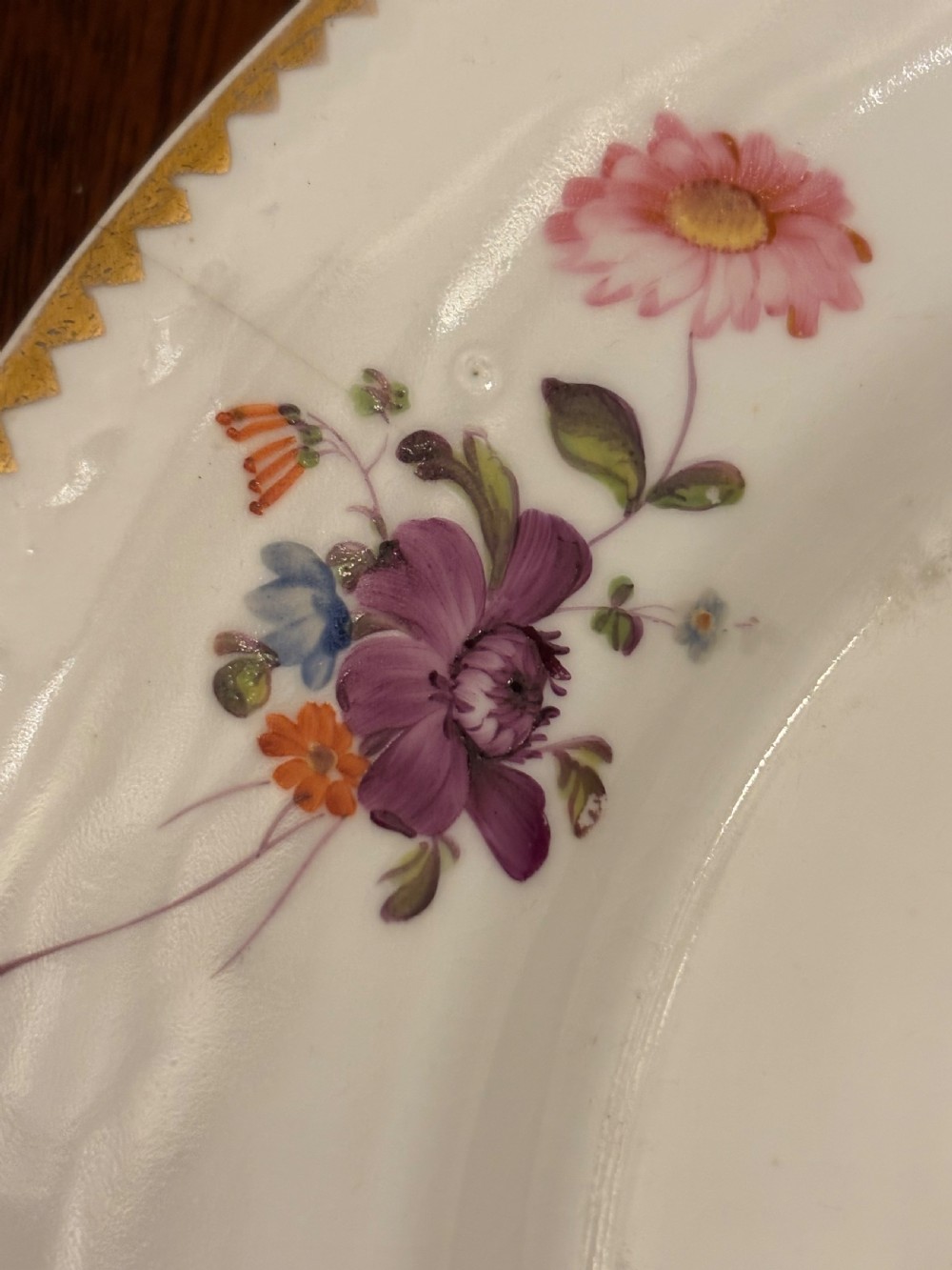 An antique off-white porcelain dessert service with hand-painted floral sprigs, scalloped edges, and gilded rims arranged against a black backdrop. View IV