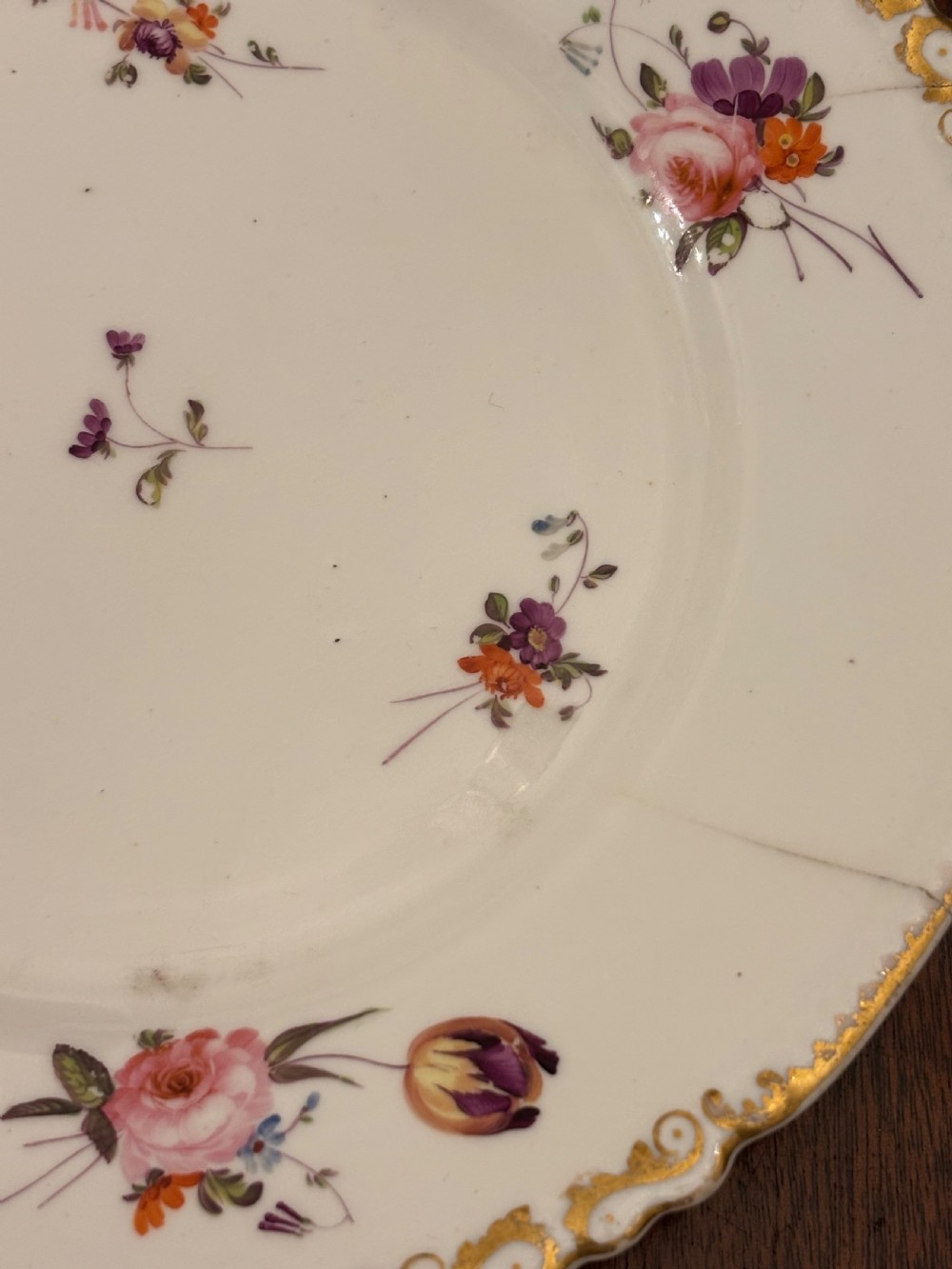 An antique off-white porcelain dessert service with hand-painted floral sprigs, scalloped edges, and gilded rims arranged against a black backdrop. View V