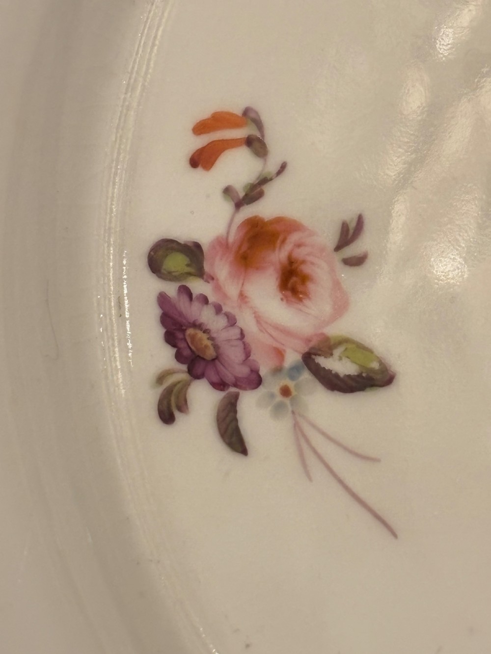 An antique off-white porcelain dessert service with hand-painted floral sprigs, scalloped edges, and gilded rims arranged against a black backdrop. View XII