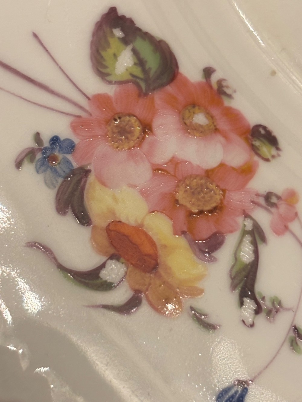 An antique off-white porcelain dessert service with hand-painted floral sprigs, scalloped edges, and gilded rims arranged against a black backdrop. View XVI