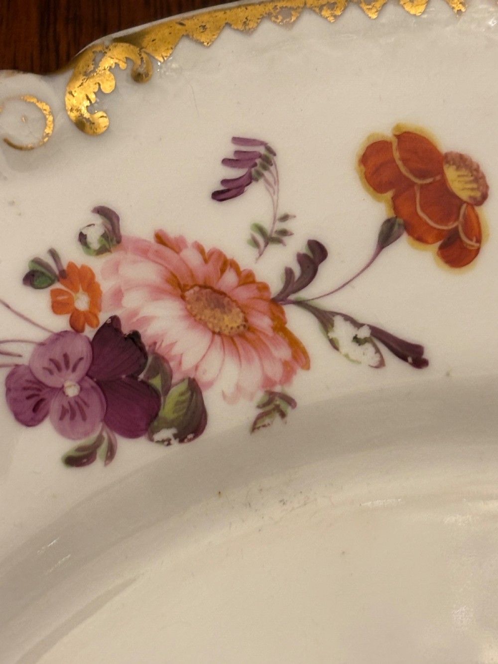 An antique off-white porcelain dessert service with hand-painted floral sprigs, scalloped edges, and gilded rims arranged against a black backdrop. View XVII