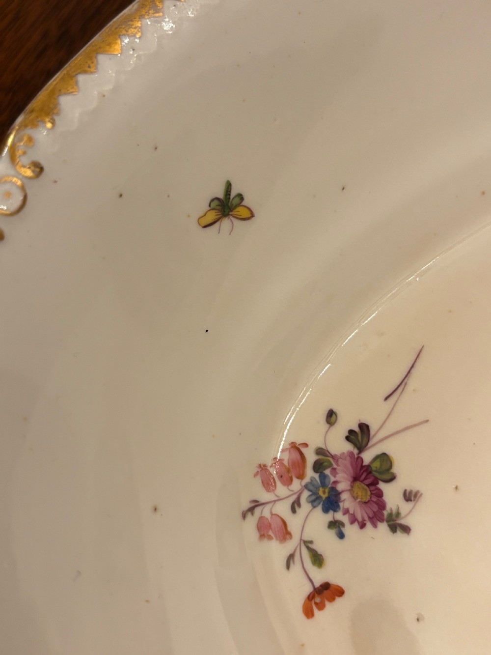 An antique off-white porcelain dessert service with hand-painted floral sprigs, scalloped edges, and gilded rims arranged against a black backdrop. View XXI