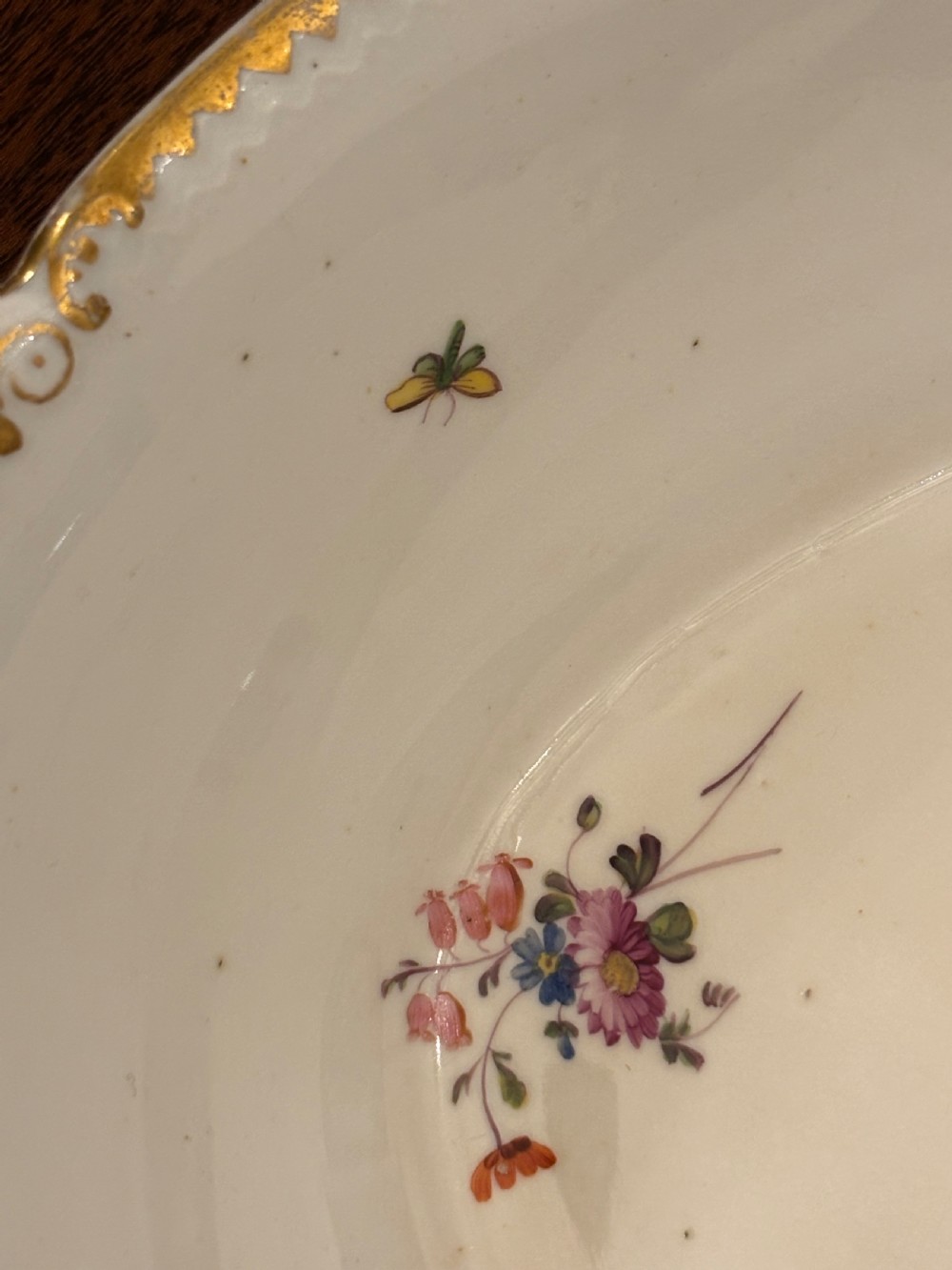 An antique off-white porcelain dessert service with hand-painted floral sprigs, scalloped edges, and gilded rims arranged against a black backdrop. View XXII