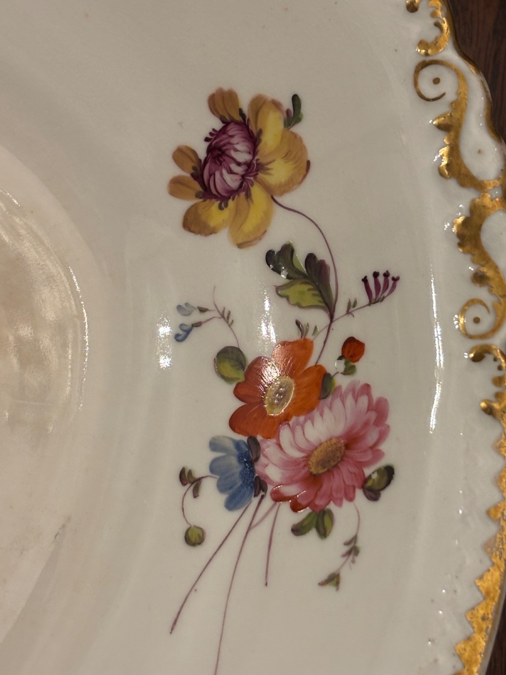 An antique off-white porcelain dessert service with hand-painted floral sprigs, scalloped edges, and gilded rims arranged against a black backdrop. View XXIII