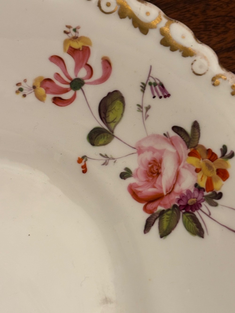 An antique off-white porcelain dessert service with hand-painted floral sprigs, scalloped edges, and gilded rims arranged against a black backdrop. View XXVII