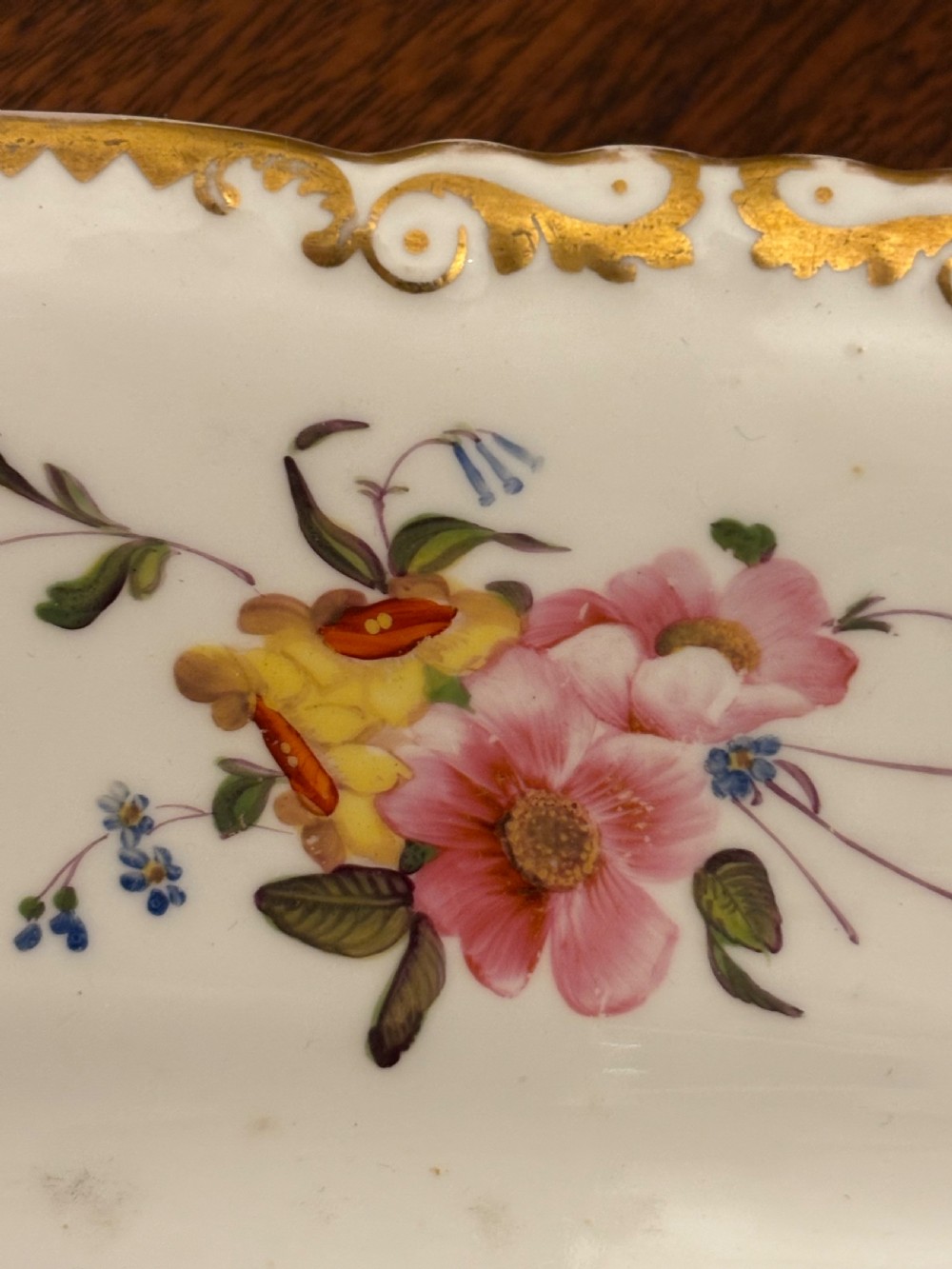 An antique off-white porcelain dessert service with hand-painted floral sprigs, scalloped edges, and gilded rims arranged against a black backdrop. View XXVIII