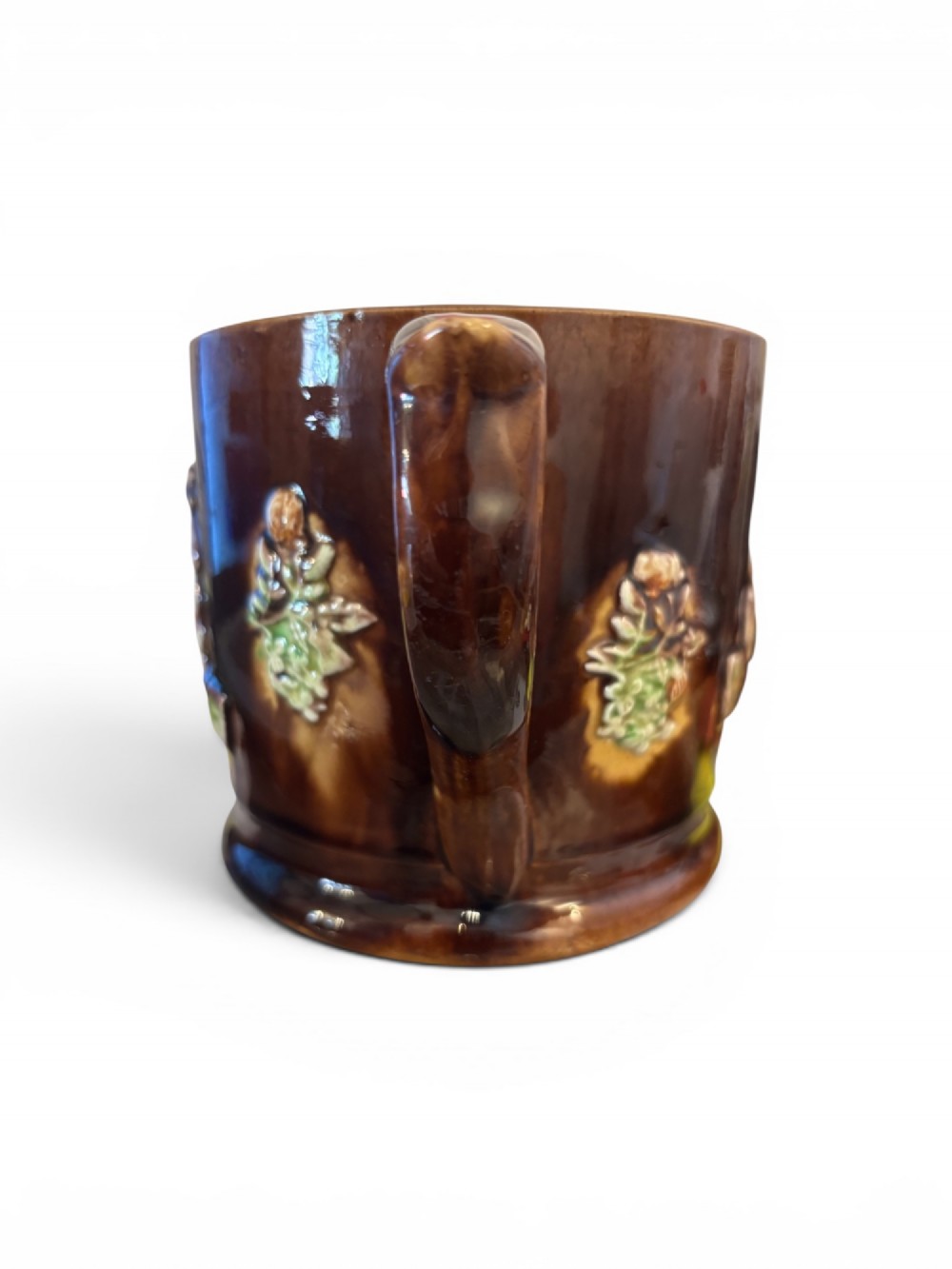 A dark brown glazed earthenware two-handled tankard featuring raised relief moulding of a seated figure drinking at a table. View IV