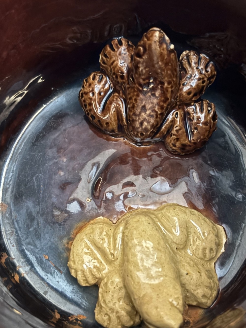 A dark brown glazed earthenware two-handled tankard featuring raised relief moulding of a seated figure drinking at a table. View V