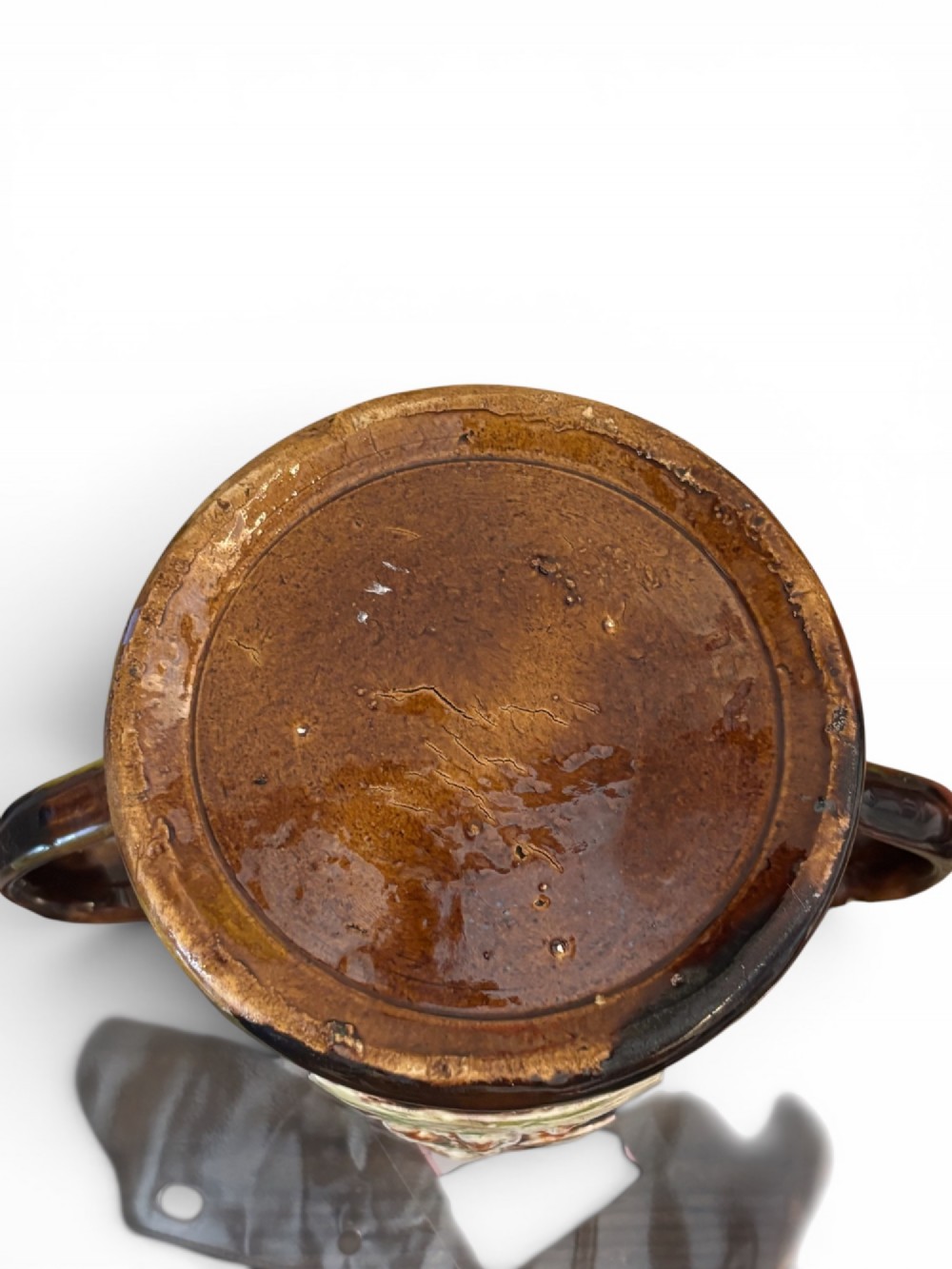 A dark brown glazed earthenware two-handled tankard featuring raised relief moulding of a seated figure drinking at a table. View VI
