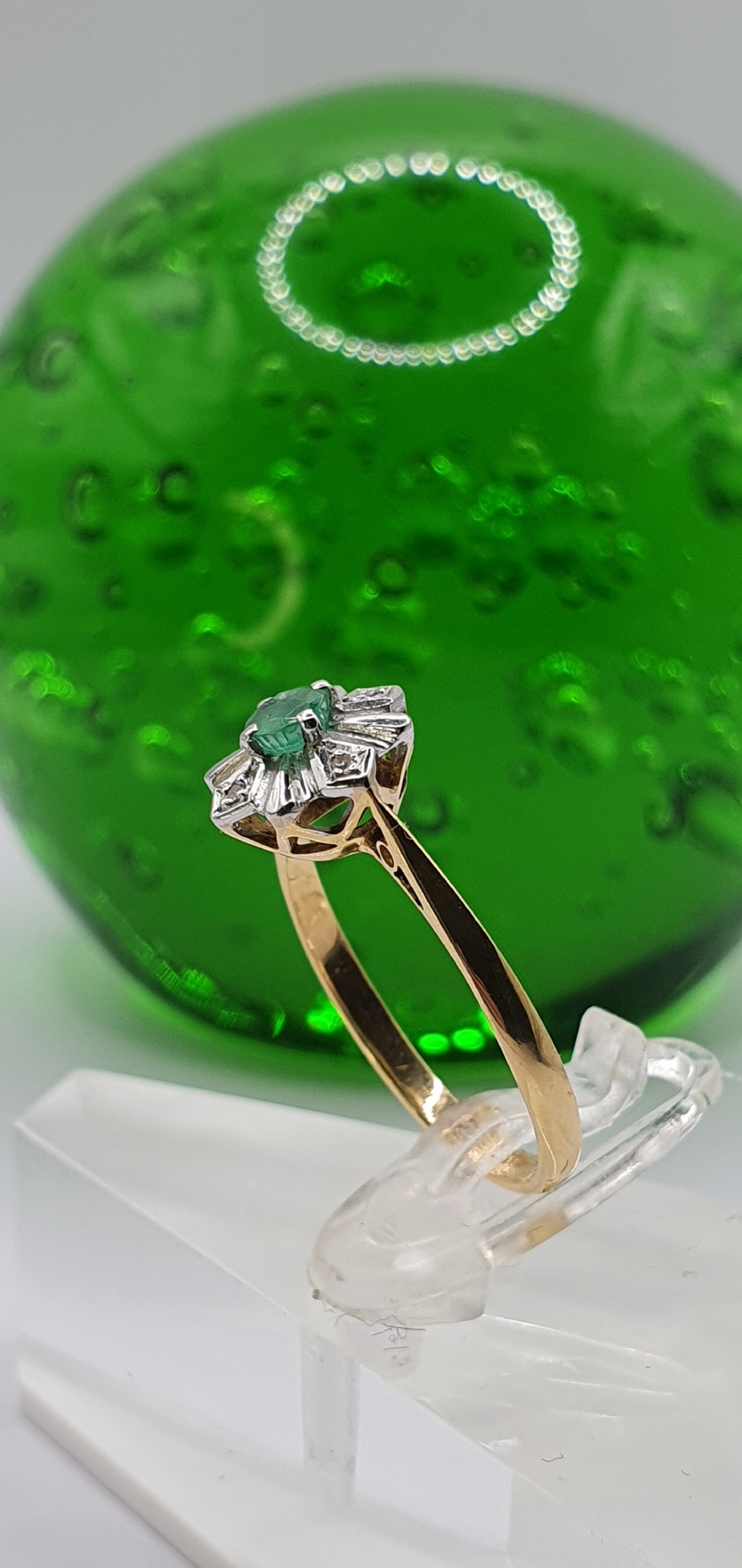 An 18ct yellow gold Art Deco ring featuring a central round green emerald set within a starburst cluster setting with diamond accents. View VII