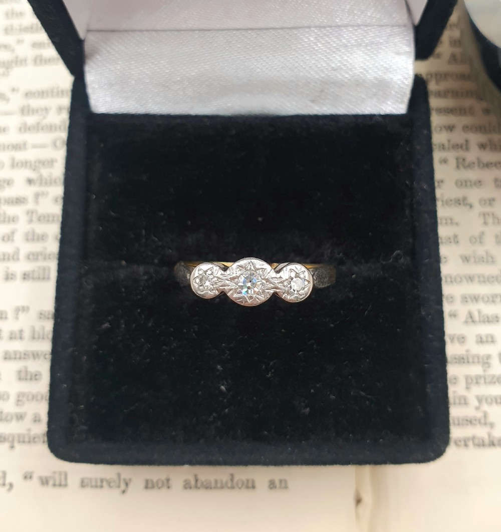 An Art Deco trilogy ring featuring three star-set round diamonds in a platinum setting on an 18ct yellow gold band.