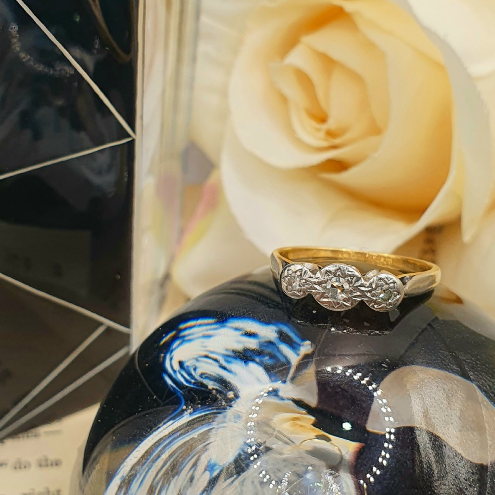An Art Deco trilogy ring featuring three star-set round diamonds in a platinum setting on an 18ct yellow gold band. View V