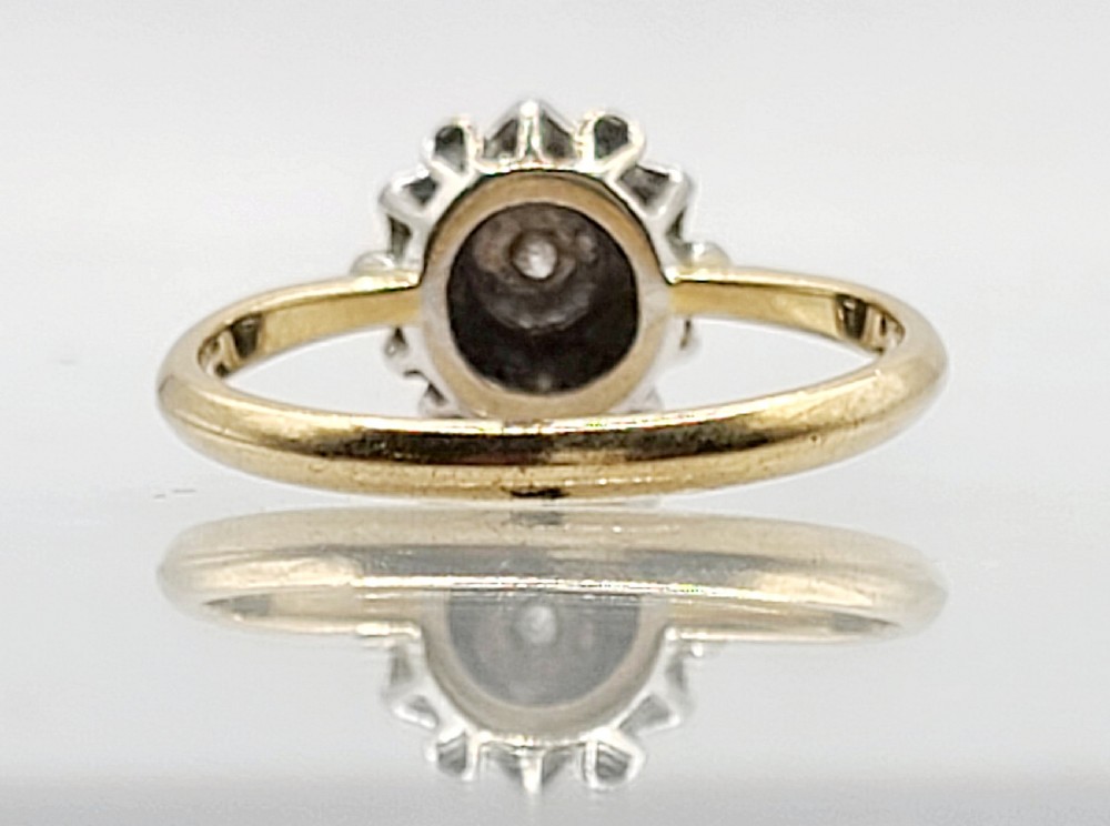 A vintage 18ct yellow gold and white metal cluster ring featuring a central diamond surrounded by a floral halo of smaller diamonds. View V