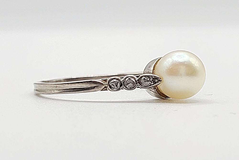Top-down view of an 18ct gold Art Deco ring featuring a central round pearl flanked by small diamonds set along the shoulders. View IV