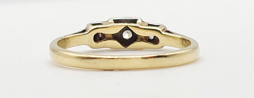 An Art Deco platinum-set and 18ct gold trilogy diamond ring featuring three central stones within a geometric bezel and millgrained border. View V