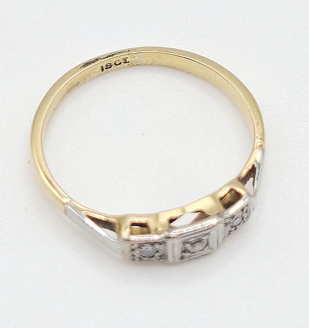 An Art Deco platinum-set and 18ct gold trilogy diamond ring featuring three central stones within a geometric bezel and millgrained border. View VI