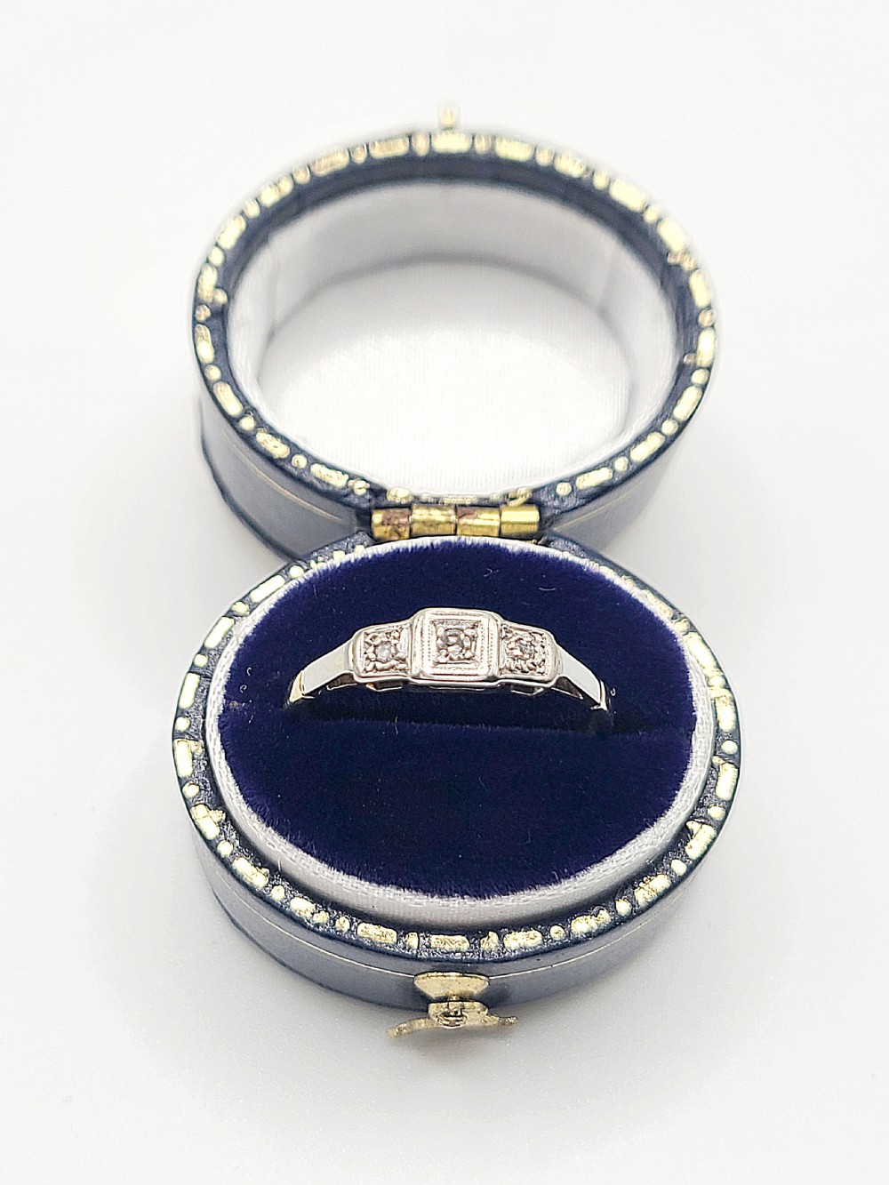 An Art Deco platinum-set and 18ct gold trilogy diamond ring featuring three central stones within a geometric bezel and millgrained border. View VII