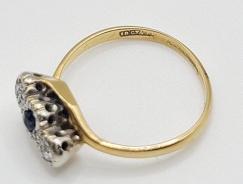 An Art Deco trilogy twist ring featuring a central round blue sapphire flanked by two diamonds set in platinum atop an 18ct yellow gold band. View VI