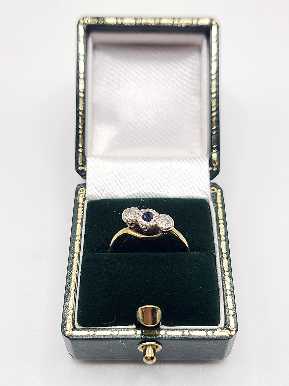 An Art Deco trilogy twist ring featuring a central round blue sapphire flanked by two diamonds set in platinum atop an 18ct yellow gold band. View VIII