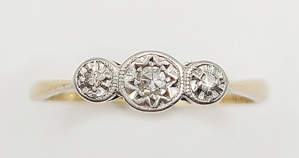 An Art Deco trilogy ring featuring three round diamonds set in star-shaped illusion palladium settings atop a yellow gold band.
