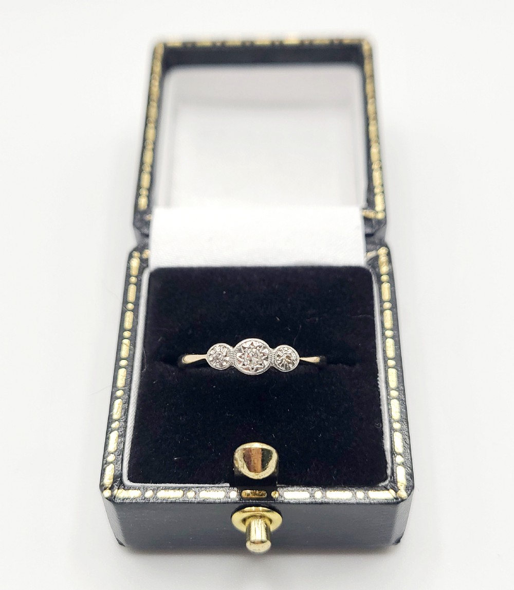 An Art Deco trilogy ring featuring three round diamonds set in star-shaped illusion palladium settings atop a yellow gold band. View VIII
