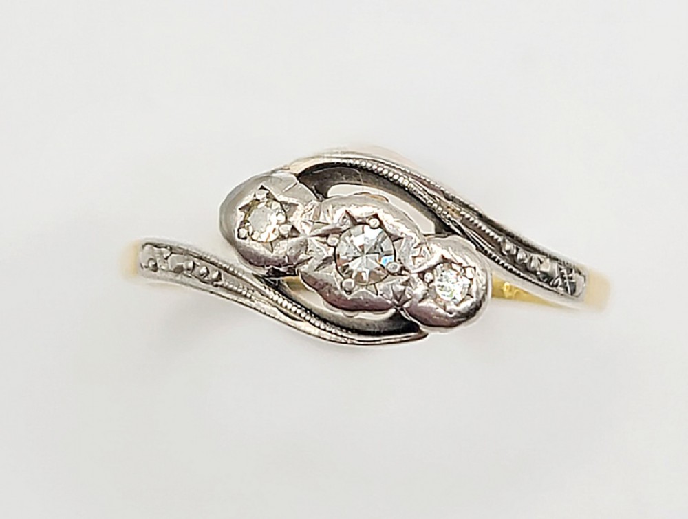 An Art Deco trilogy ring featuring three diamonds set in a platinum bypass mount on an 18ct yellow gold band.