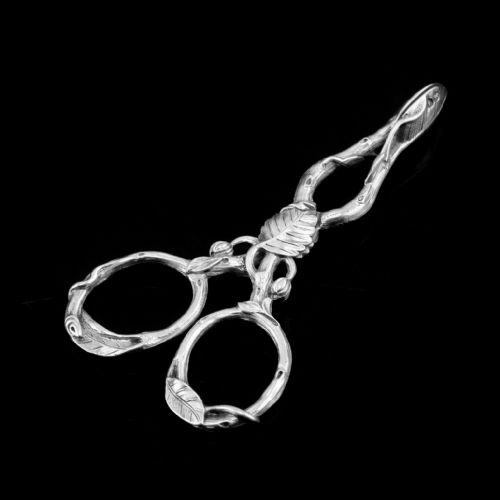 fig 1. A pair of Victorian sterling silver scissor-action sugar nips crafted in a detailed branch and leaf design against a black background.