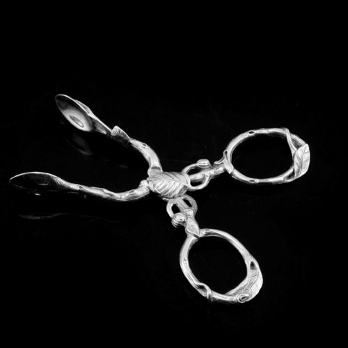fig 2. A pair of Victorian sterling silver scissor-action sugar nips crafted in a detailed branch and leaf design against a black background.