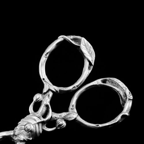 fig 3. A pair of Victorian sterling silver scissor-action sugar nips crafted in a detailed branch and leaf design against a black background.