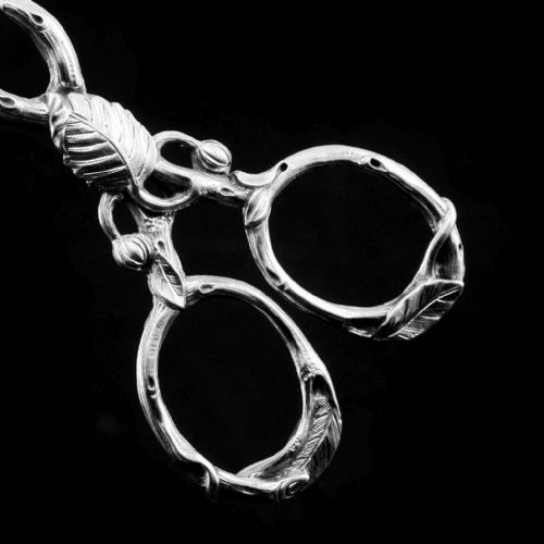 fig 4. A pair of Victorian sterling silver scissor-action sugar nips crafted in a detailed branch and leaf design against a black background.