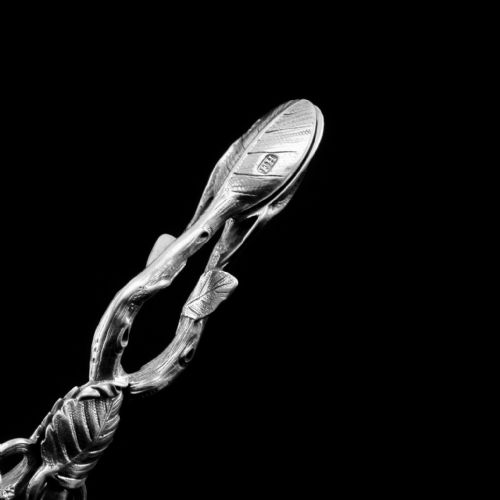 fig 5. A pair of Victorian sterling silver scissor-action sugar nips crafted in a detailed branch and leaf design against a black background.