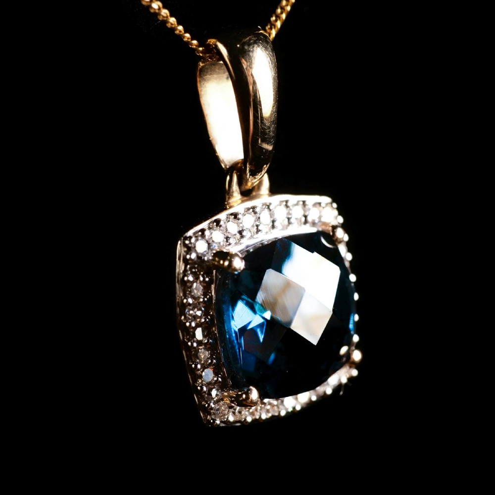A cushion-cut deep blue topaz gemstone set in a square diamond halo pendant on a gold chain. View V