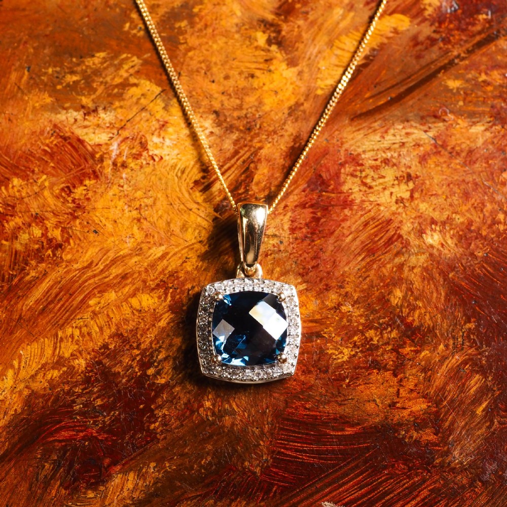 A cushion-cut deep blue topaz gemstone set in a square diamond halo pendant on a gold chain. View VII