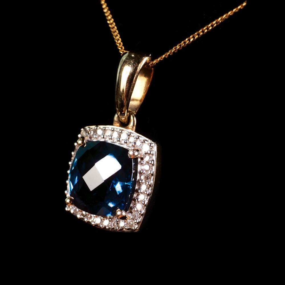 A cushion-cut deep blue topaz gemstone set in a square diamond halo pendant on a gold chain. View XIII