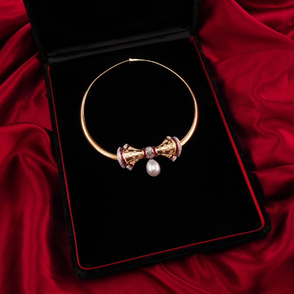 A structured 18k yellow gold collar necklace featuring a central bow motif accented with rubies and star-set diamonds above a teardrop pearl. View II