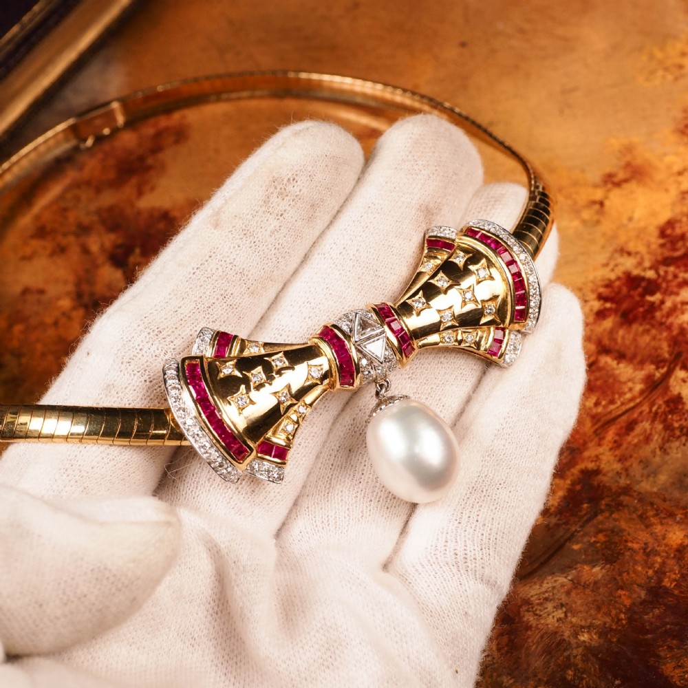 A structured 18k yellow gold collar necklace featuring a central bow motif accented with rubies and star-set diamonds above a teardrop pearl. View IV