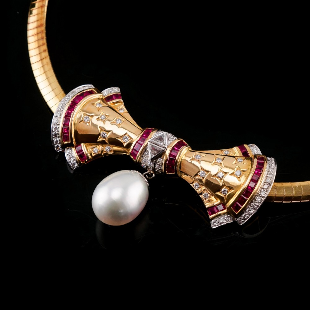 A structured 18k yellow gold collar necklace featuring a central bow motif accented with rubies and star-set diamonds above a teardrop pearl. View IX
