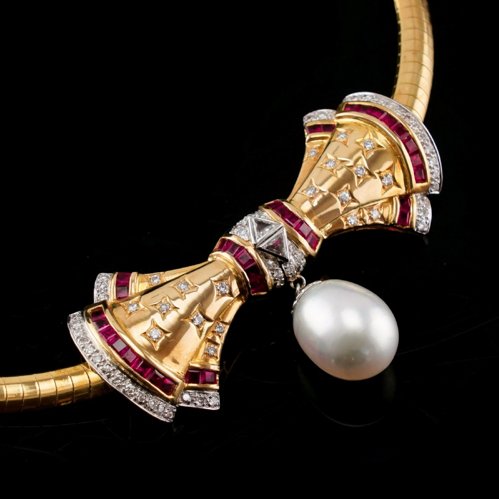 A structured 18k yellow gold collar necklace featuring a central bow motif accented with rubies and star-set diamonds above a teardrop pearl. View XI