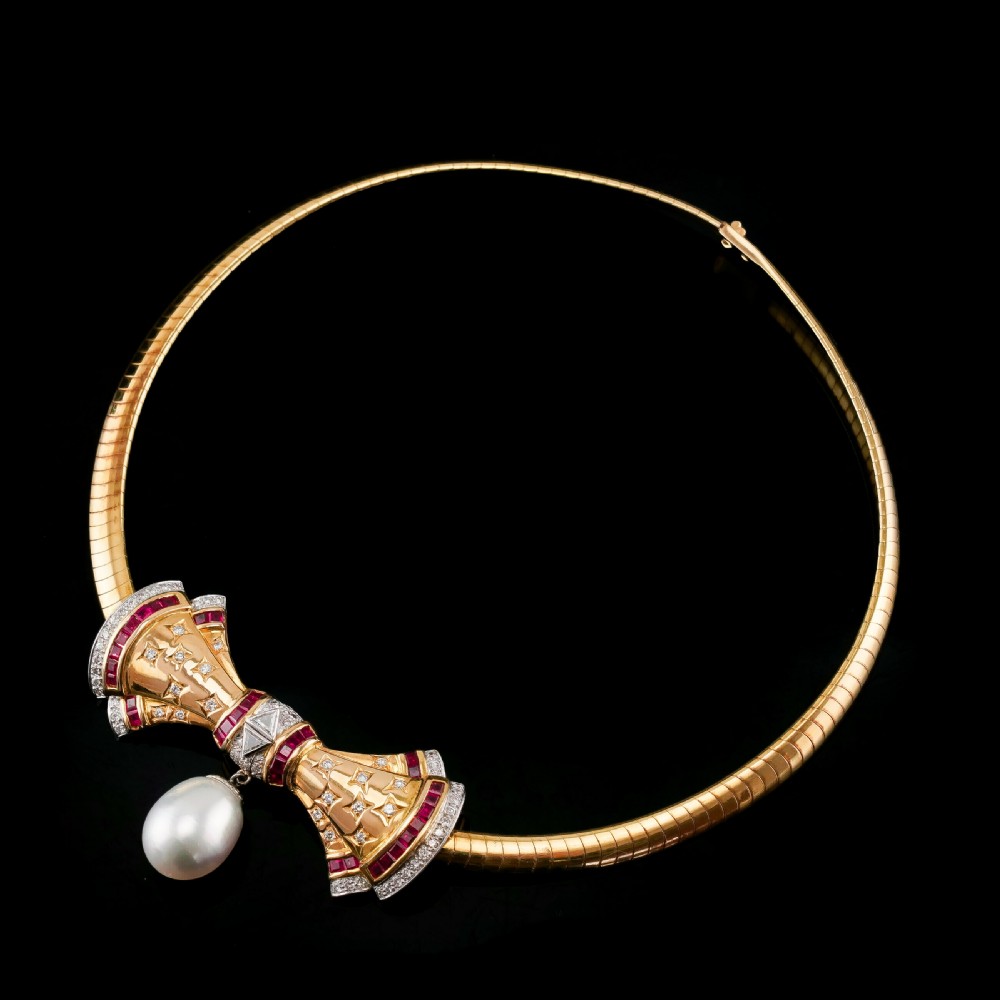 A structured 18k yellow gold collar necklace featuring a central bow motif accented with rubies and star-set diamonds above a teardrop pearl. View XII