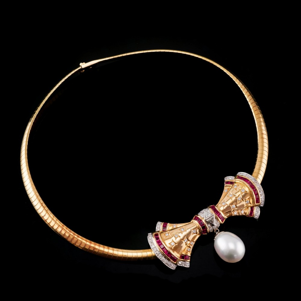 A structured 18k yellow gold collar necklace featuring a central bow motif accented with rubies and star-set diamonds above a teardrop pearl. View XIII