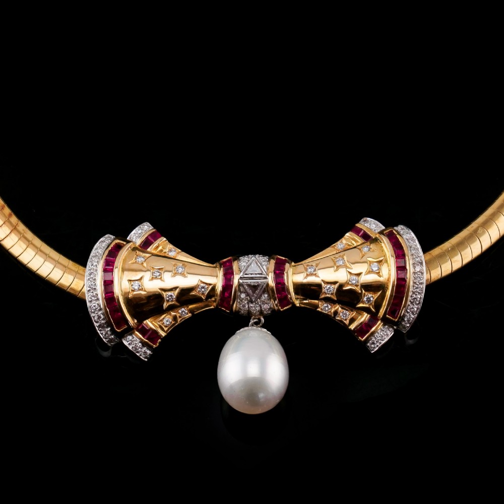 A structured 18k yellow gold collar necklace featuring a central bow motif accented with rubies and star-set diamonds above a teardrop pearl. View XIV